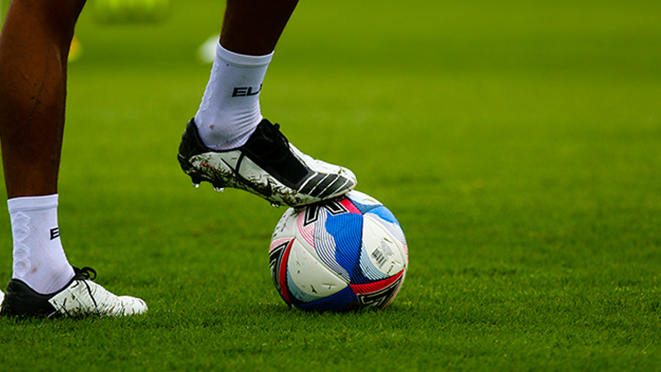 A footballer's legs and boots and a football on grass